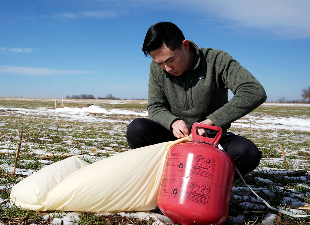 Edward Ge uses a helium tank to inflate a balloon